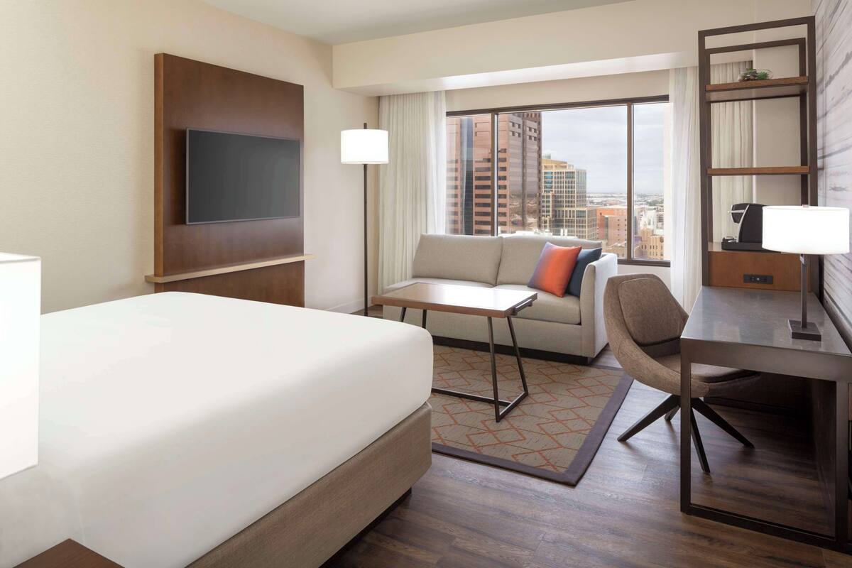 A hotel room with a bed, a sofa, a desk, and a TV.