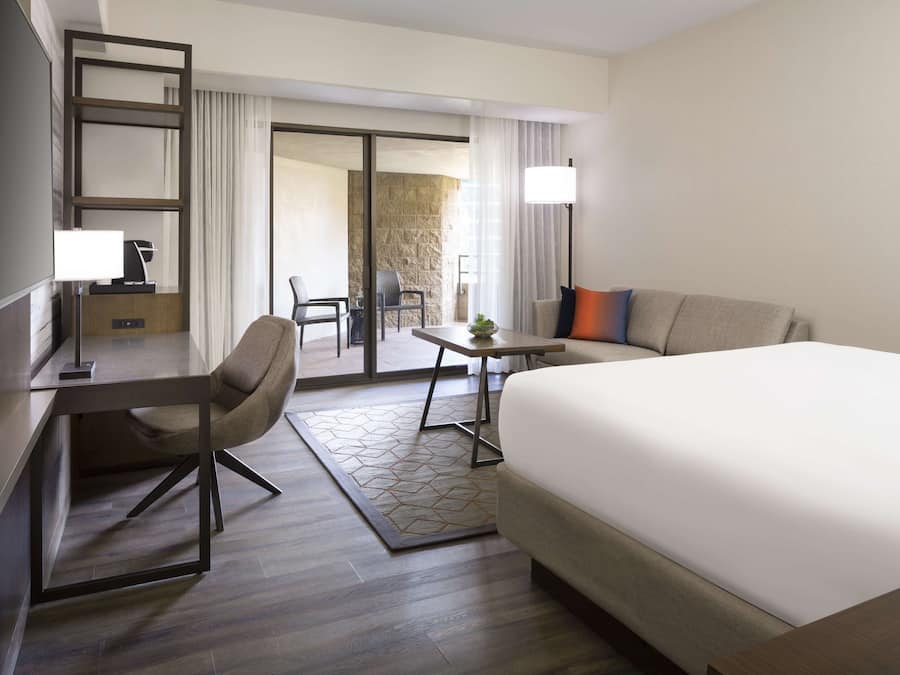 Quarto de hotel com cama, escrivaninha, cadeira, mesa pequena e vista para o exterior.