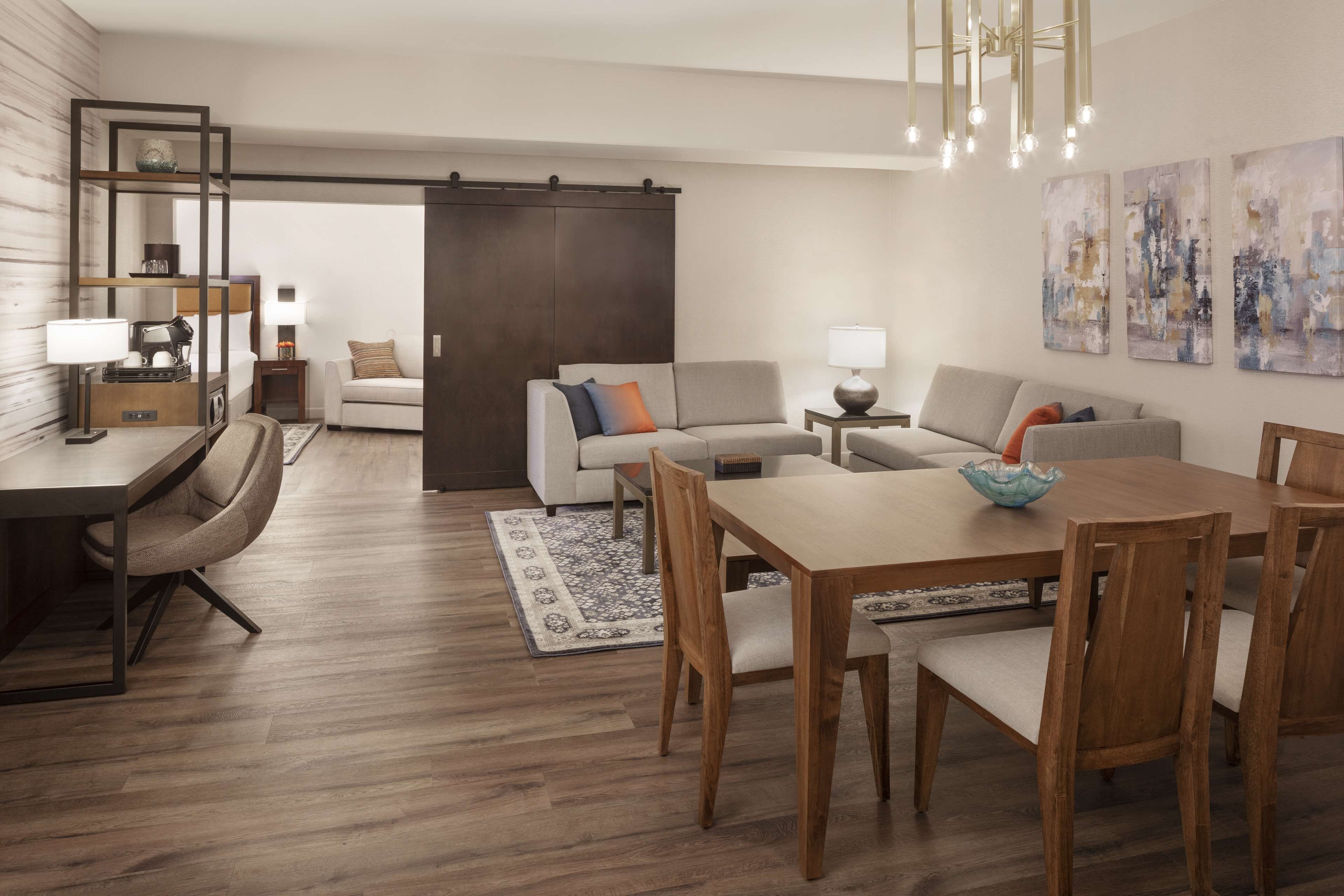 A modern living room with a dining area, a sofa, a coffee table, and a chandelier.