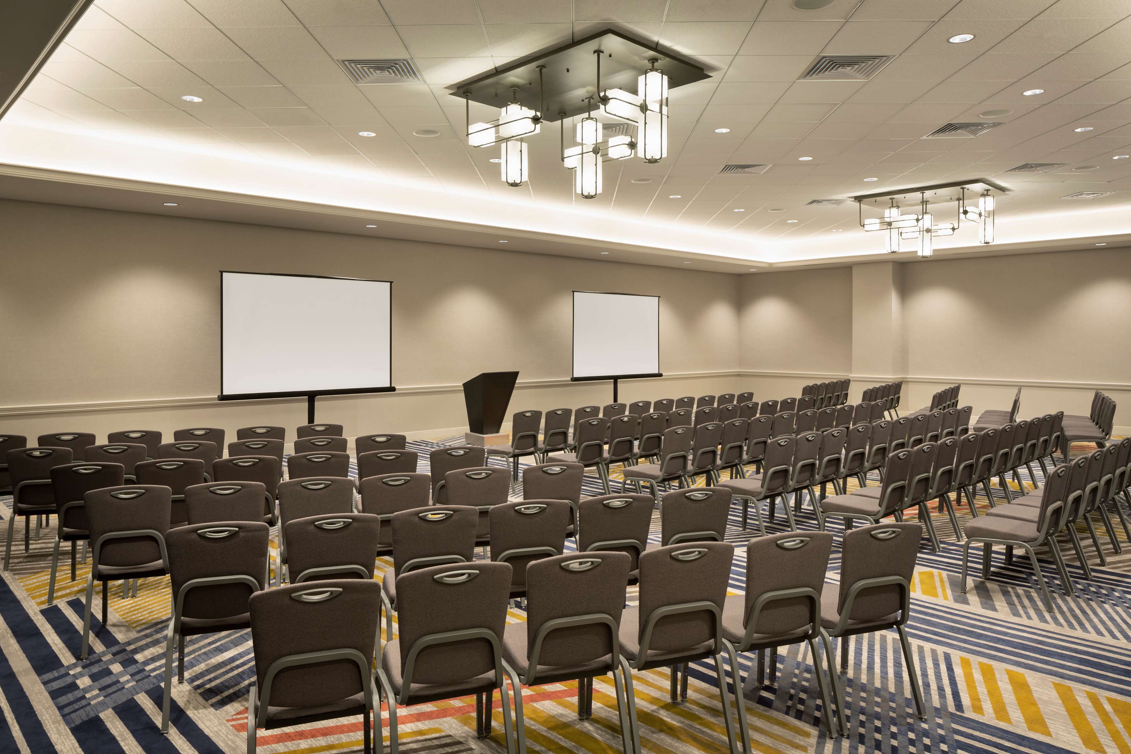 A conference room with rows of chairs, a projector screen, and a carpeted floor.