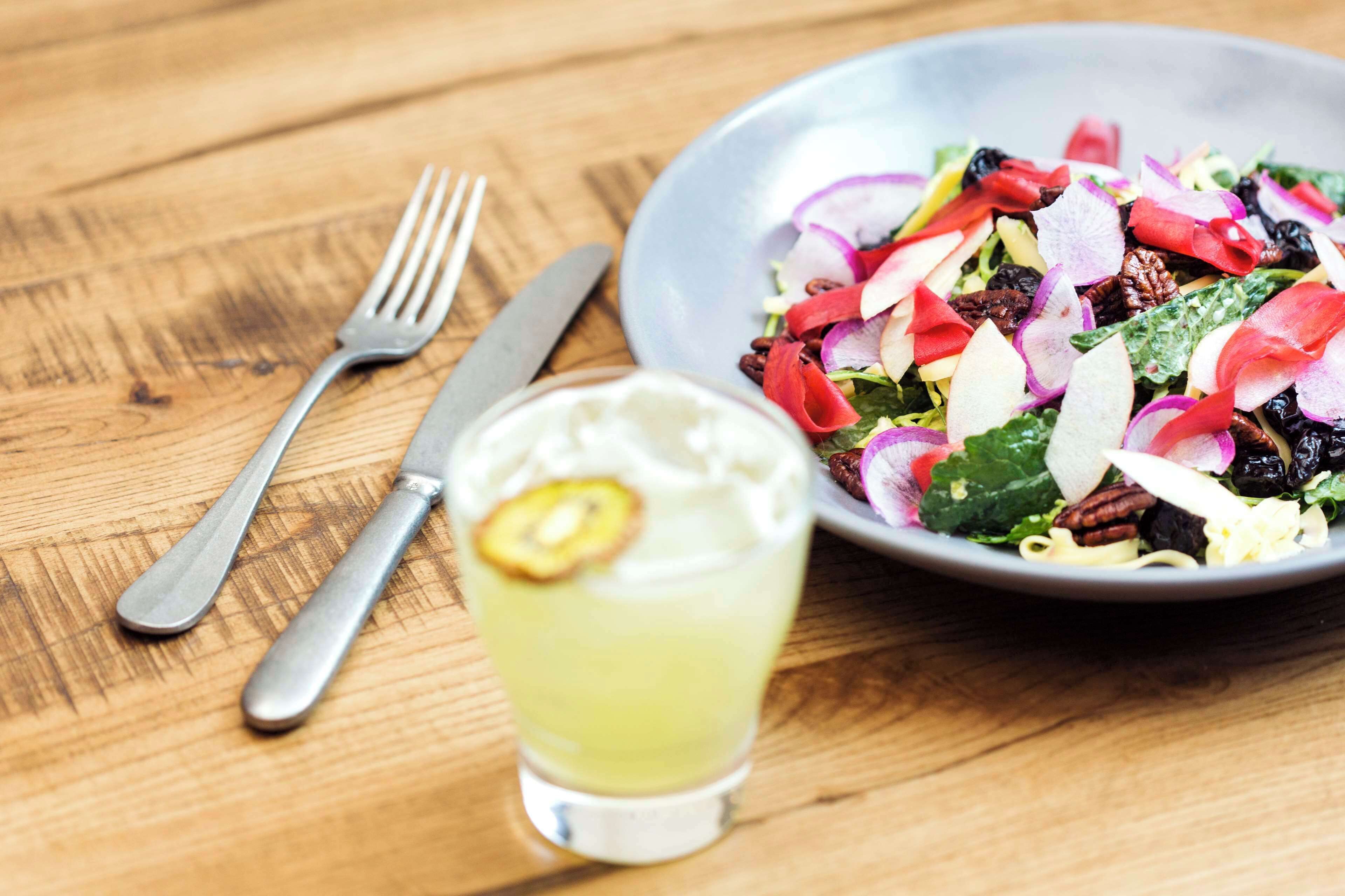 Une table en bois avec une assiette de salade, un verre et des couverts.