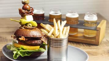 En hamburgare med bacon, ost och inlagd gurka, serverad på ett bröd, tillsammans med en portion pommes frites och fyra ölglas på ett bricka.