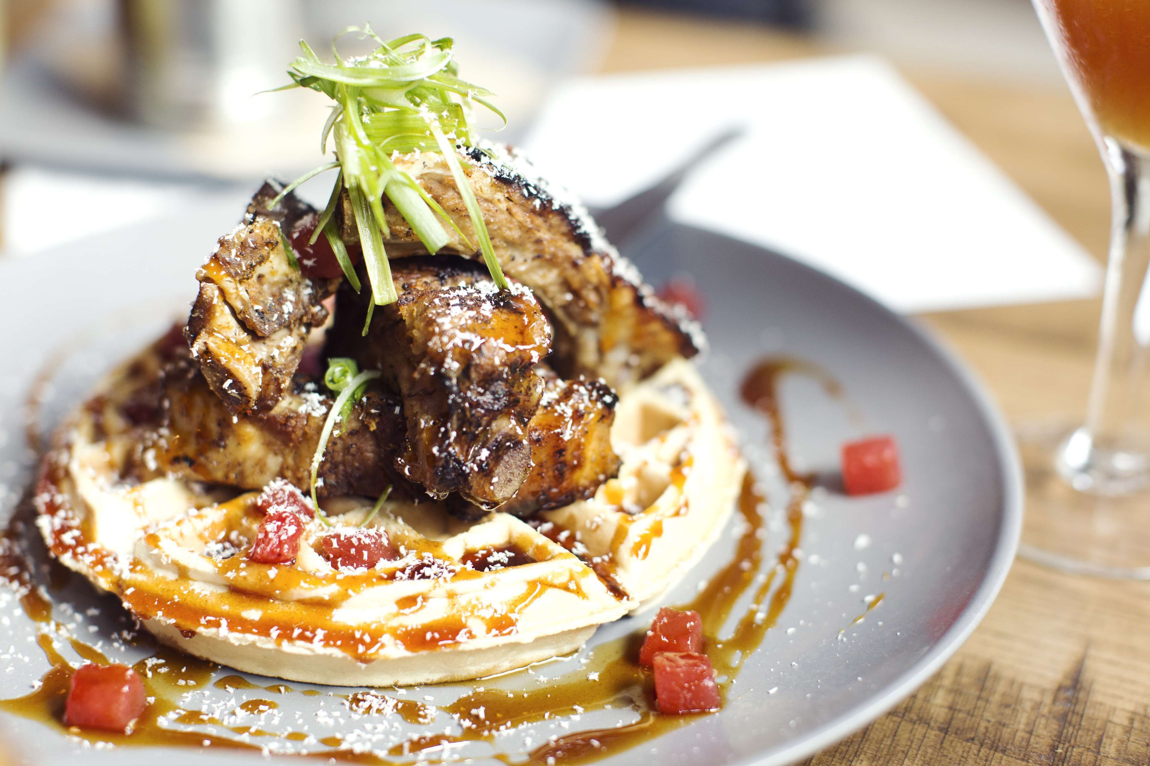 A plate of food with a waffle, meat, and garnishes.