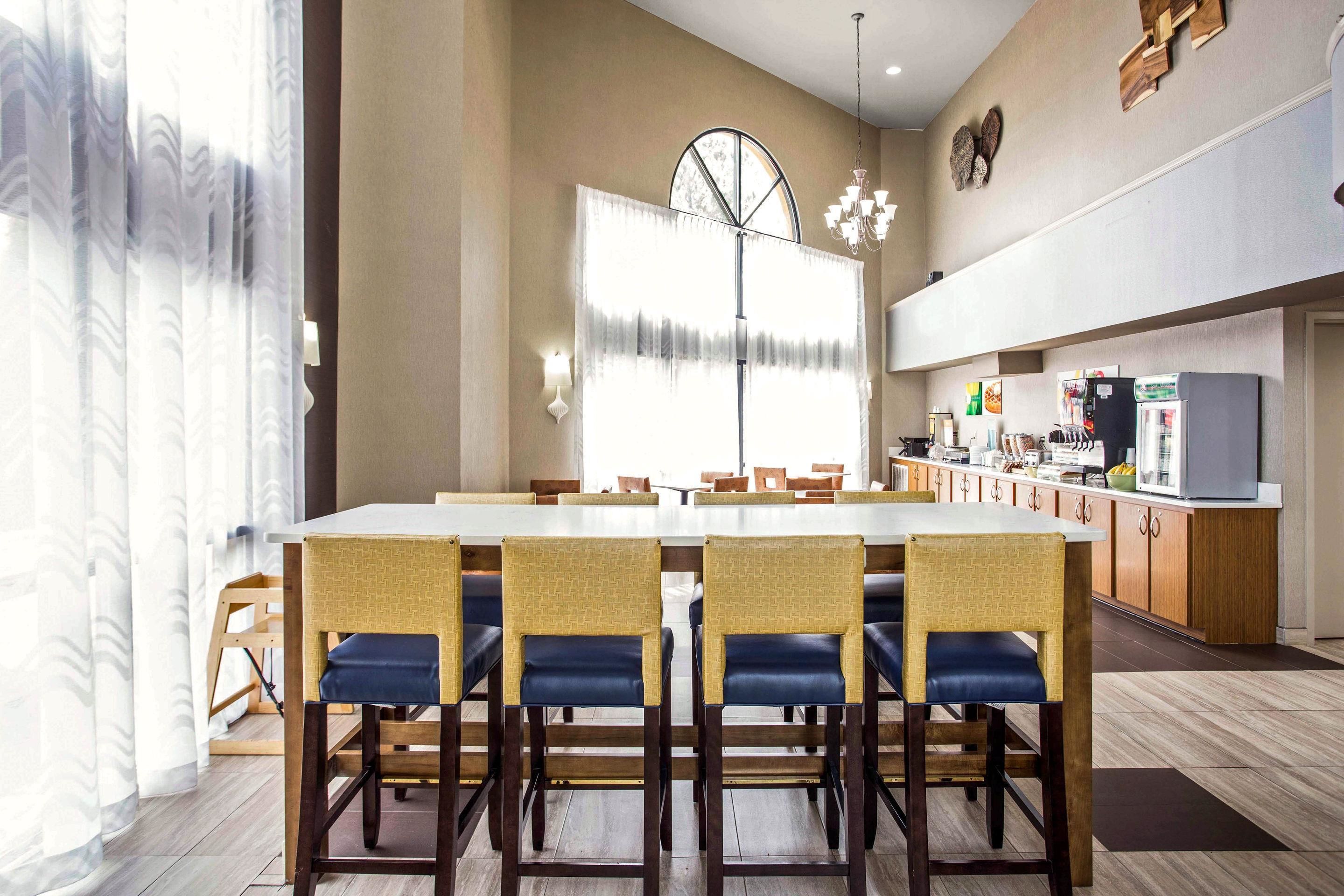 Un comedor con una mesa larga y sillas, una cocina al fondo y un ventanal con cortinas.