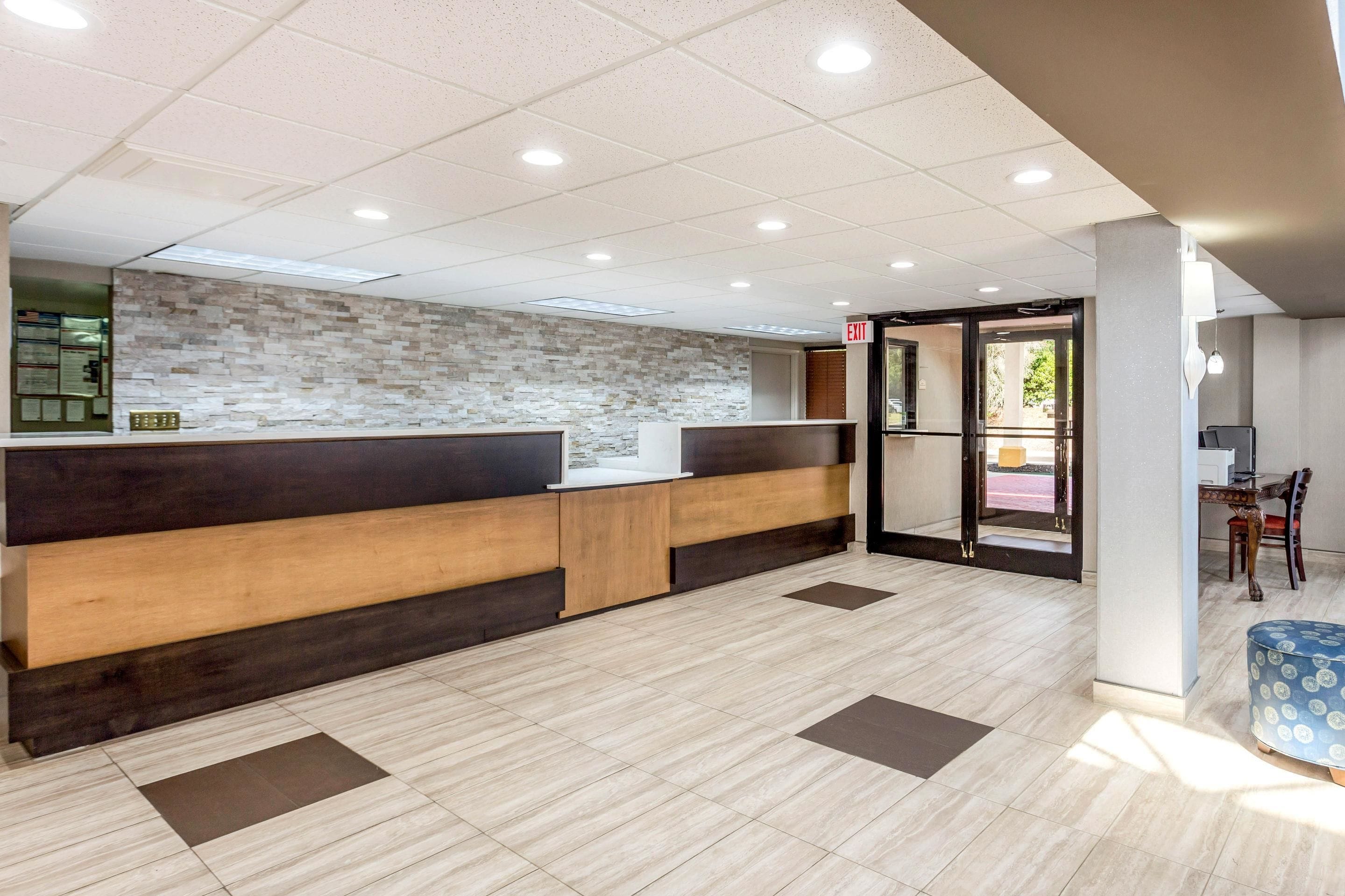 A reception area with a modern design, featuring a wooden reception desk, a stone wall, and a tiled floor.