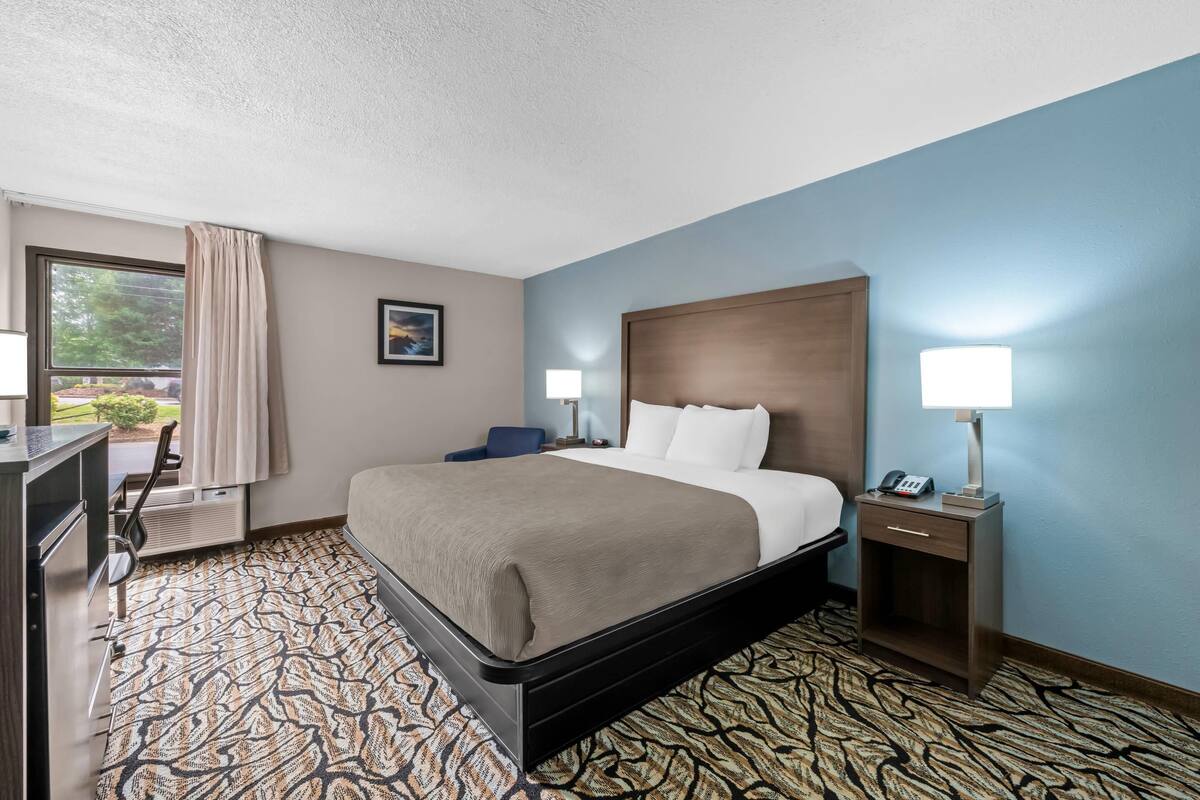 A hotel room with a bed, bedside lamps, a desk, and a chair.