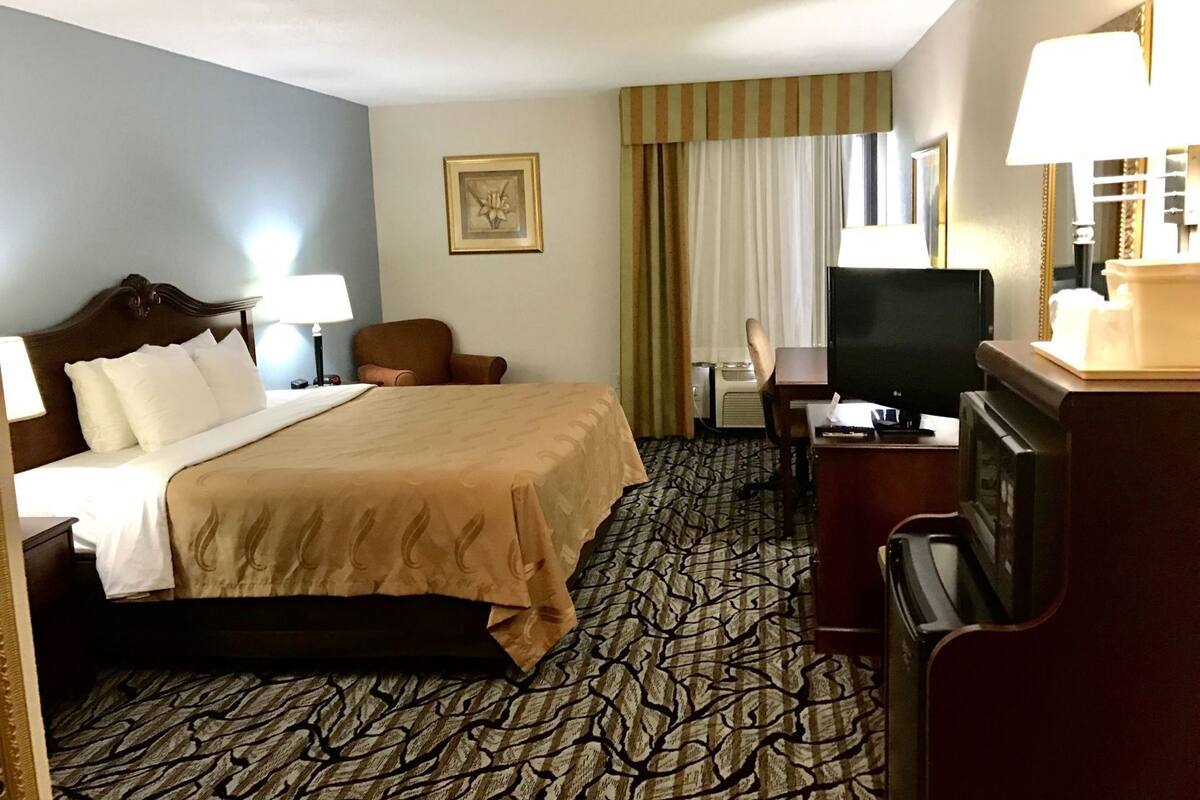 A hotel room with a bed, a desk, a chair, a television, and a window with curtains.