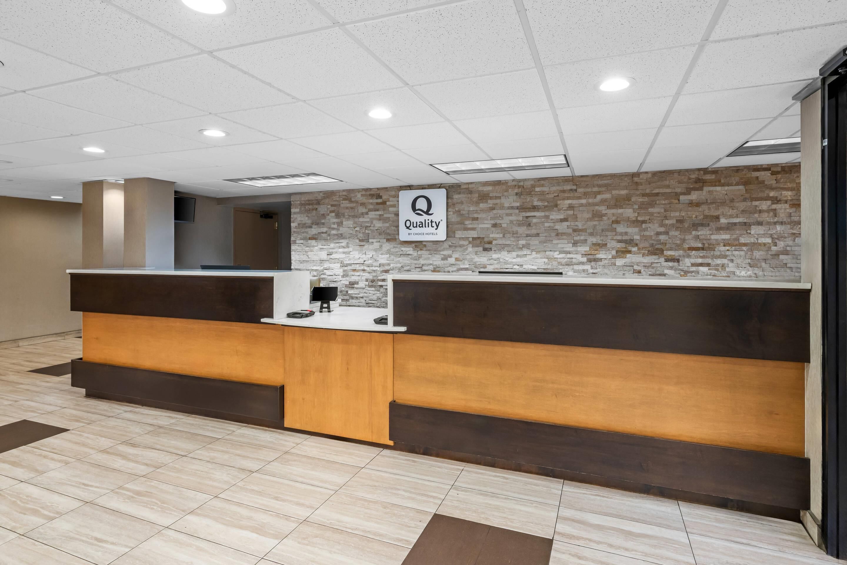 A reception desk with a 'Quality' sign, a modern design with a stone wall backdrop, and a tiled floor.