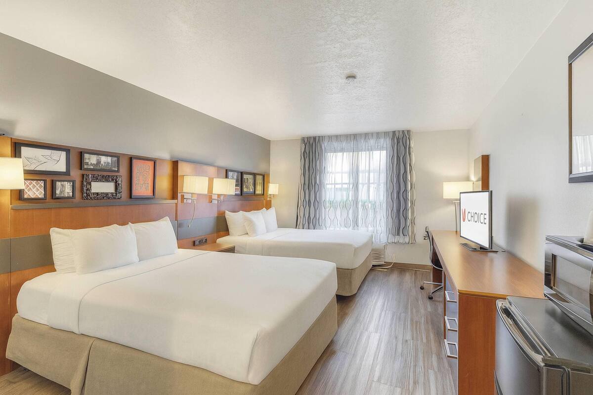 Une chambre d’hôtel avec deux lits, un bureau, une télévision et une fenêtre avec des rideaux.