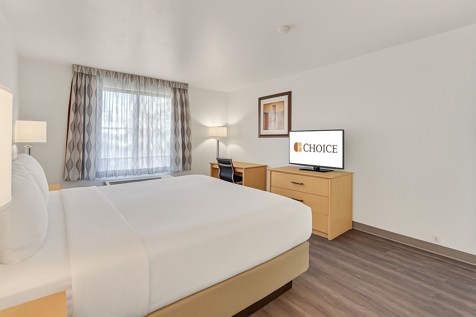 A hotel room with a large bed, a desk with a chair, a television, and a window with curtains.