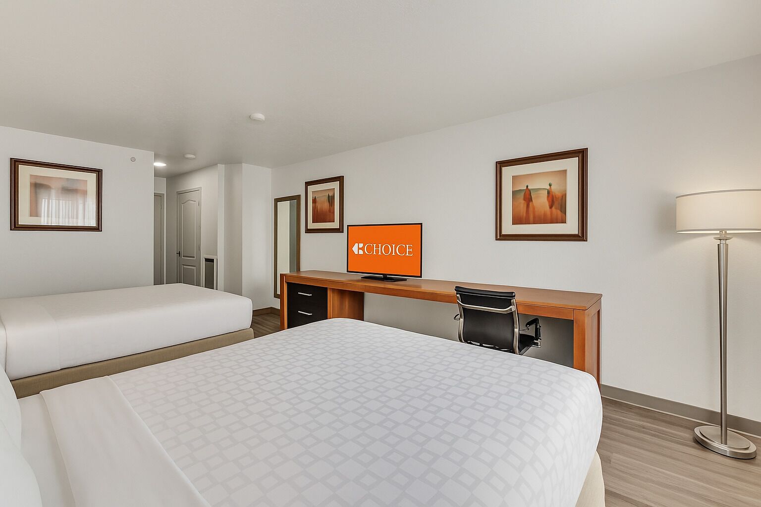 A hotel room with two beds, a desk with a computer, and a lamp.