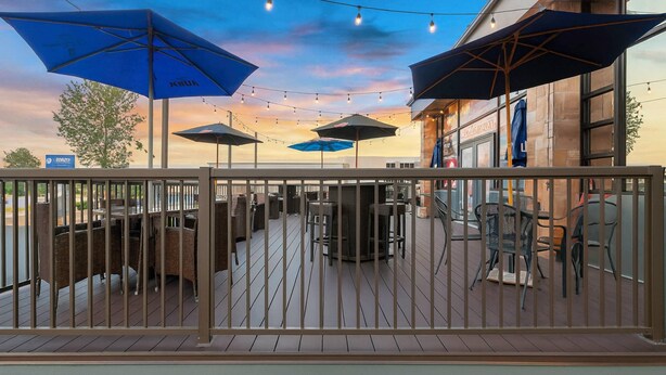 An outdoor patio with tables and chairs, blue umbrellas, and string lights against a sunset sky. - Clarion Inn Salt Lake City Airport (Salt Lake City)