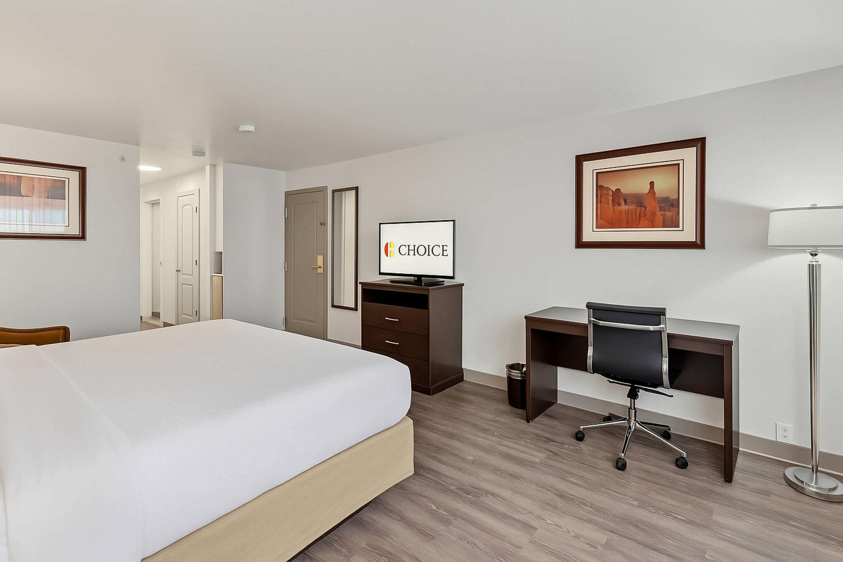 A hotel room with a bed, desk, chair, TV, and framed pictures on the wall.
