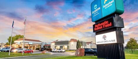 A hotel with a Suburban Studios sign, a digital sign for Amelia's Grill & Bar, and a flagpole with flags.