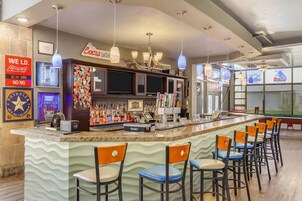 Una zona de bar con una barra larga, varios taburetes y una amplia variedad de botellas y vasos.