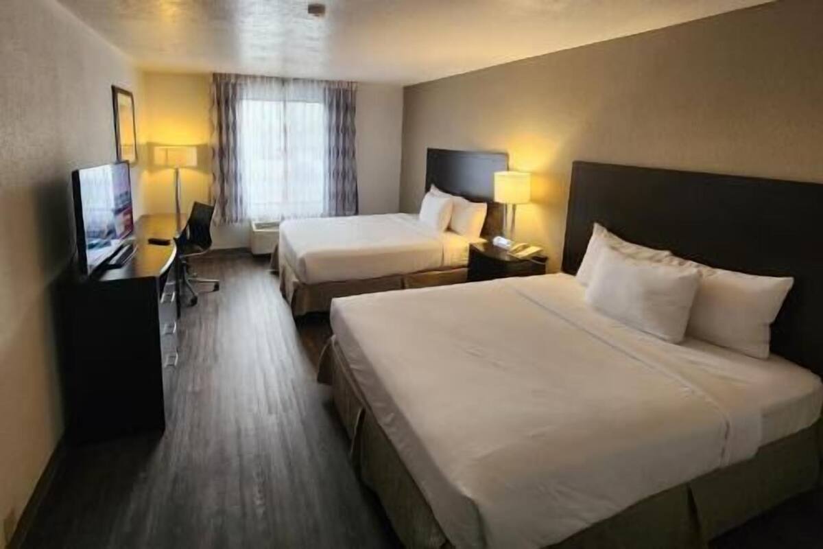 Une chambre d’hôtel avec deux lits, un bureau avec une chaise, une télévision et une fenêtre avec des rideaux.