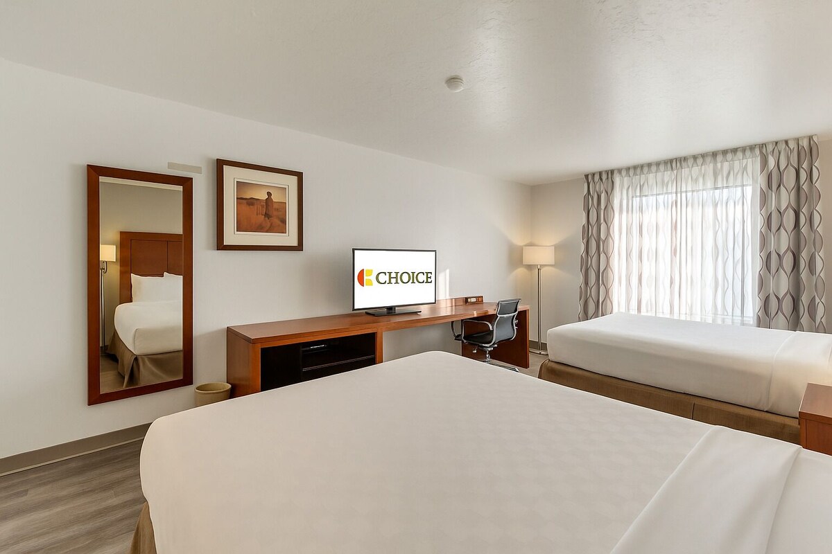 Habitación de hotel con una cama grande, un escritorio con computadora, televisión y ventana con cortinas.