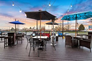 An outdoor patio with tables and chairs, umbrellas, and string lights against a sunset sky.