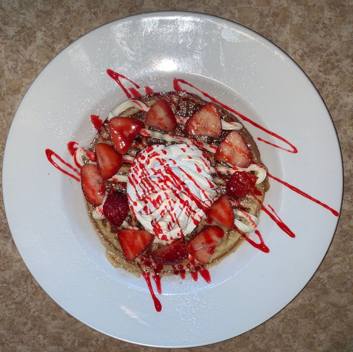 Un plato con un postre que incluye una capa base, fresas en rodajas por encima, un poco de crema y un chorrito de sirope rojo.