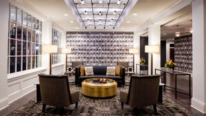 Eine geräumige Lobby mit einer zentralen Sitzecke, ausgestattet mit einer Couch und Sesseln, einem gemusterten Teppich und einer Wanddekoration mit einer Bildergalerie.