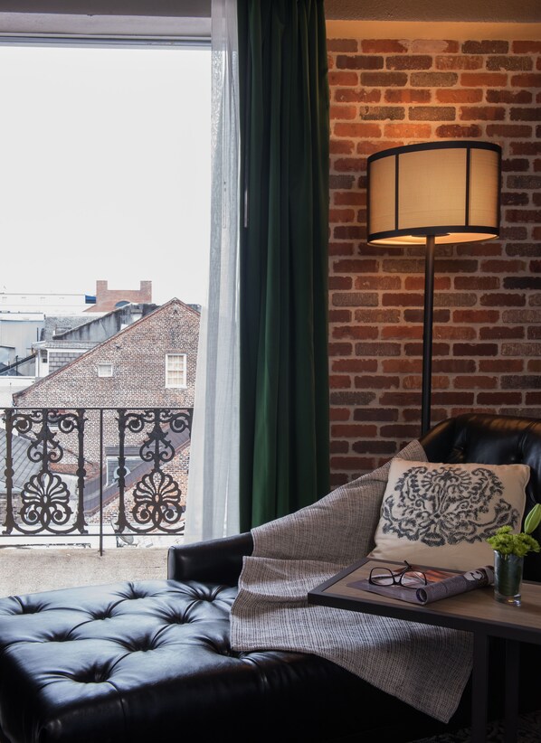 A cozy living room with a leather sofa, a patterned throw pillow, and a floor lamp against a brick wall.