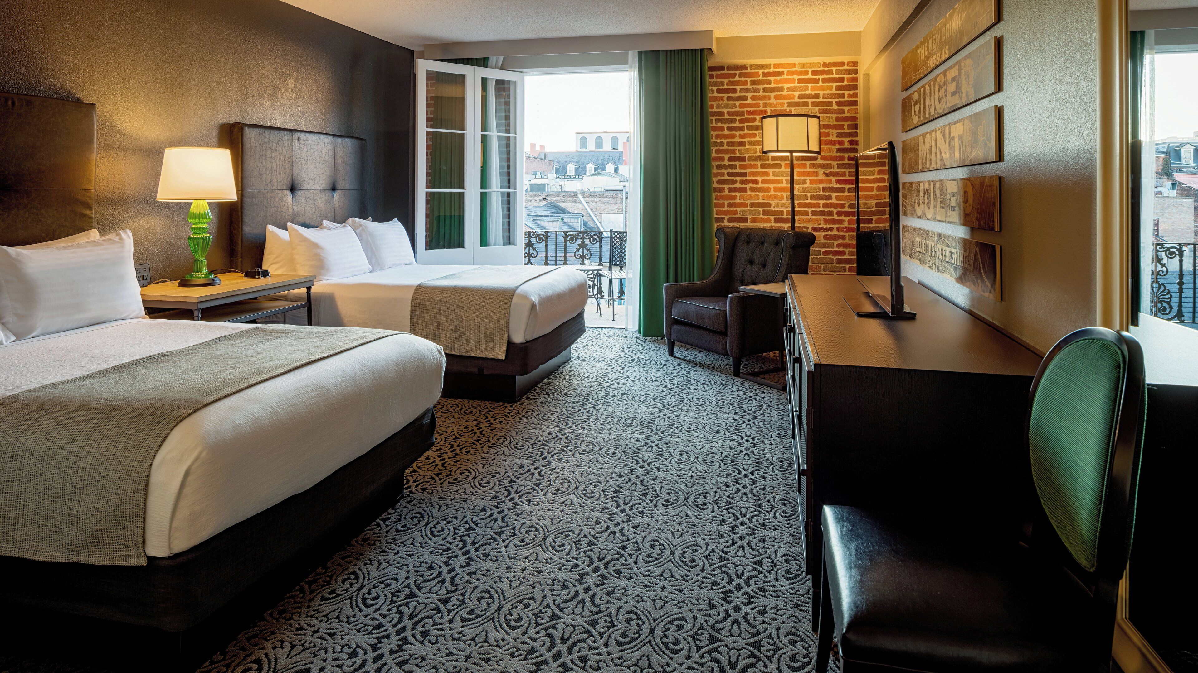 Habitación de hotel con dos camas, un escritorio, una silla, una lámpara y vistas a la ciudad.