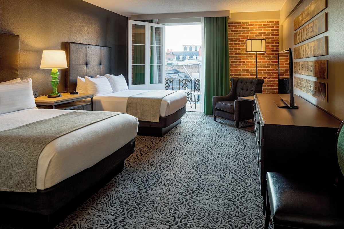 Hotelkamer met twee bedden, een bureau, een stoel, een lamp en uitzicht op de stad door het raam.