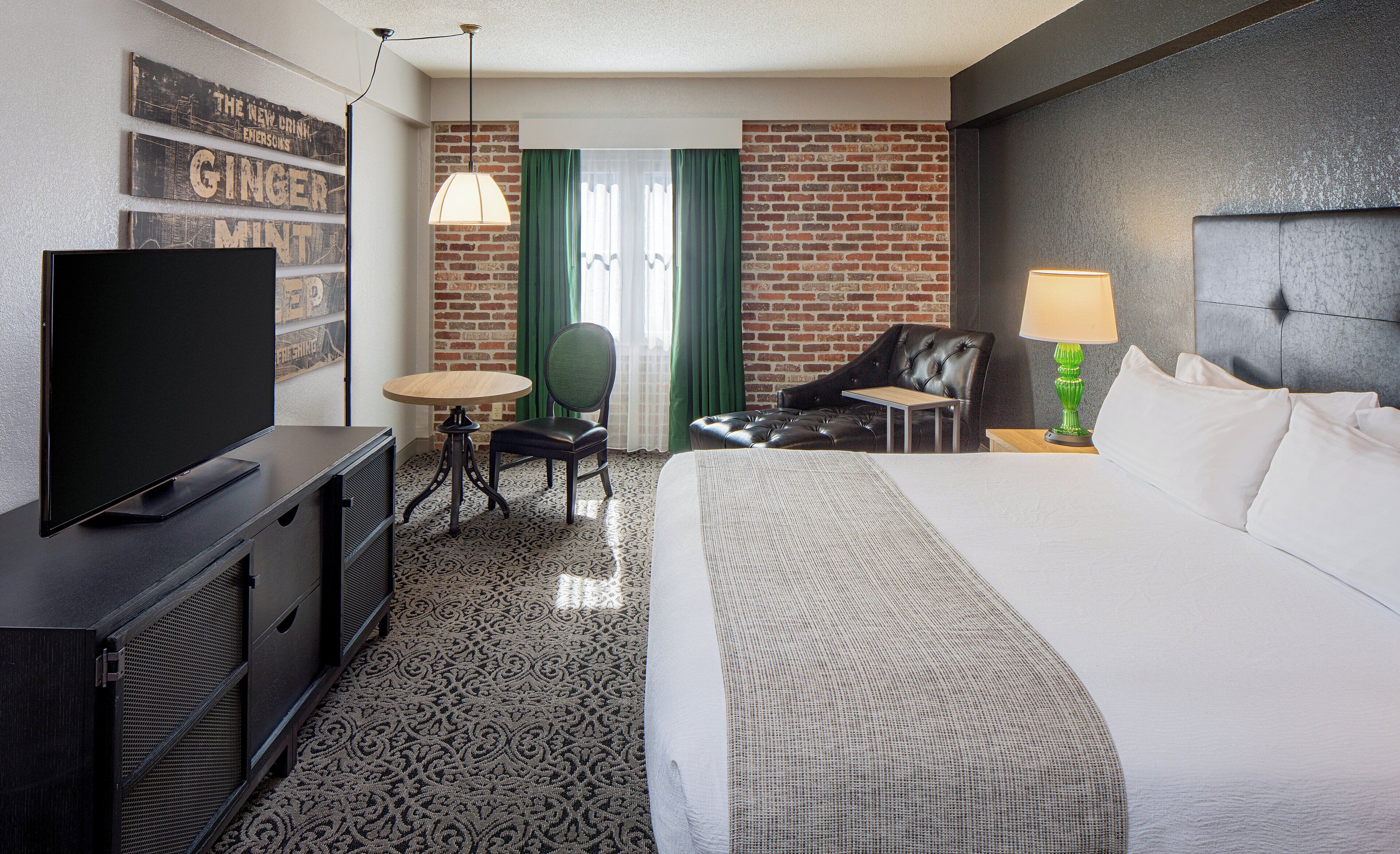 Quarto de hotel com televisão de tela plana, uma mesa redonda, uma cadeira, um sofá, um abajur e uma cama.