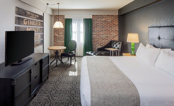 Habitación de hotel con televisión de pantalla plana, una mesa redonda, una silla, un sofá, una lámpara y una cama.