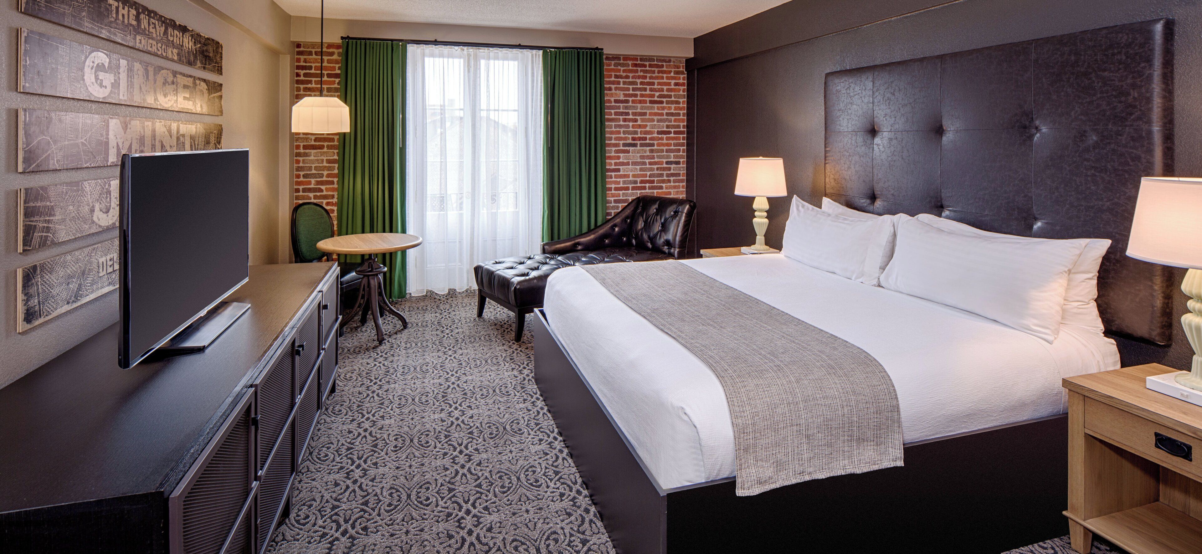 Une chambre d’hôtel équipée d’un lit, d’un bureau, d’une chaise, d’une télévision et d’une fenêtre avec des rideaux.