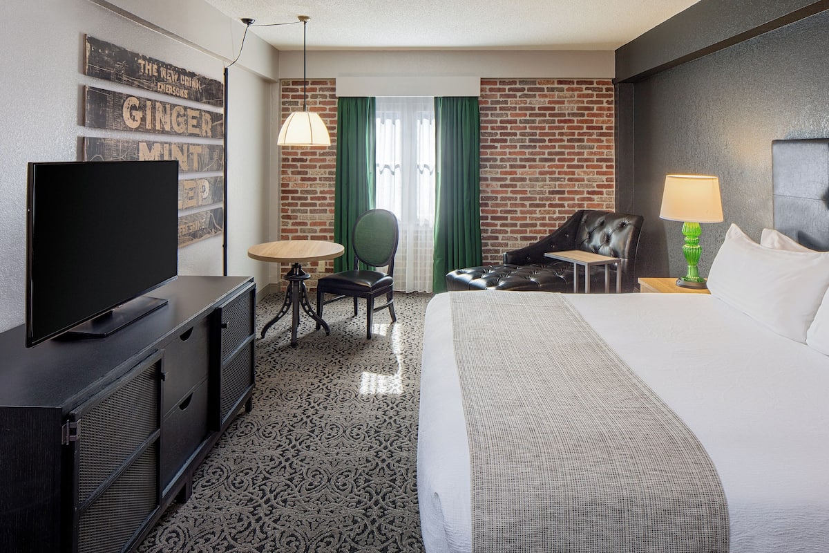 Ein Hotelzimmer mit Flachbildfernseher, rundem Tisch, Stuhl, Sofa, Lampe und einem Bett.