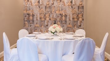 Un salón de conferencias con una mesa redonda para seis personas, sillas blancas y un centro de mesa floral.