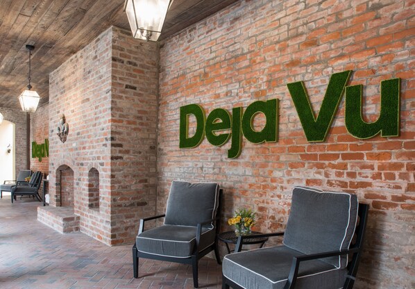 A brick wall with the words "Deja Vu" in green letters. There are two grey chairs with white piping, a small table with a vase of yellow flowers, and a brick fireplace. - Holiday Inn FRENCH QUARTER-CHATEAU LEMOYNE by IHG (New Orleans)