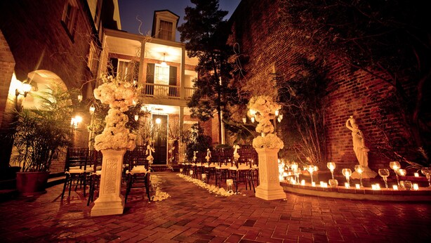 Un lieu de réception en plein air pour les mariages, avec un chemin en briques, des compositions florales blanches et une statue.