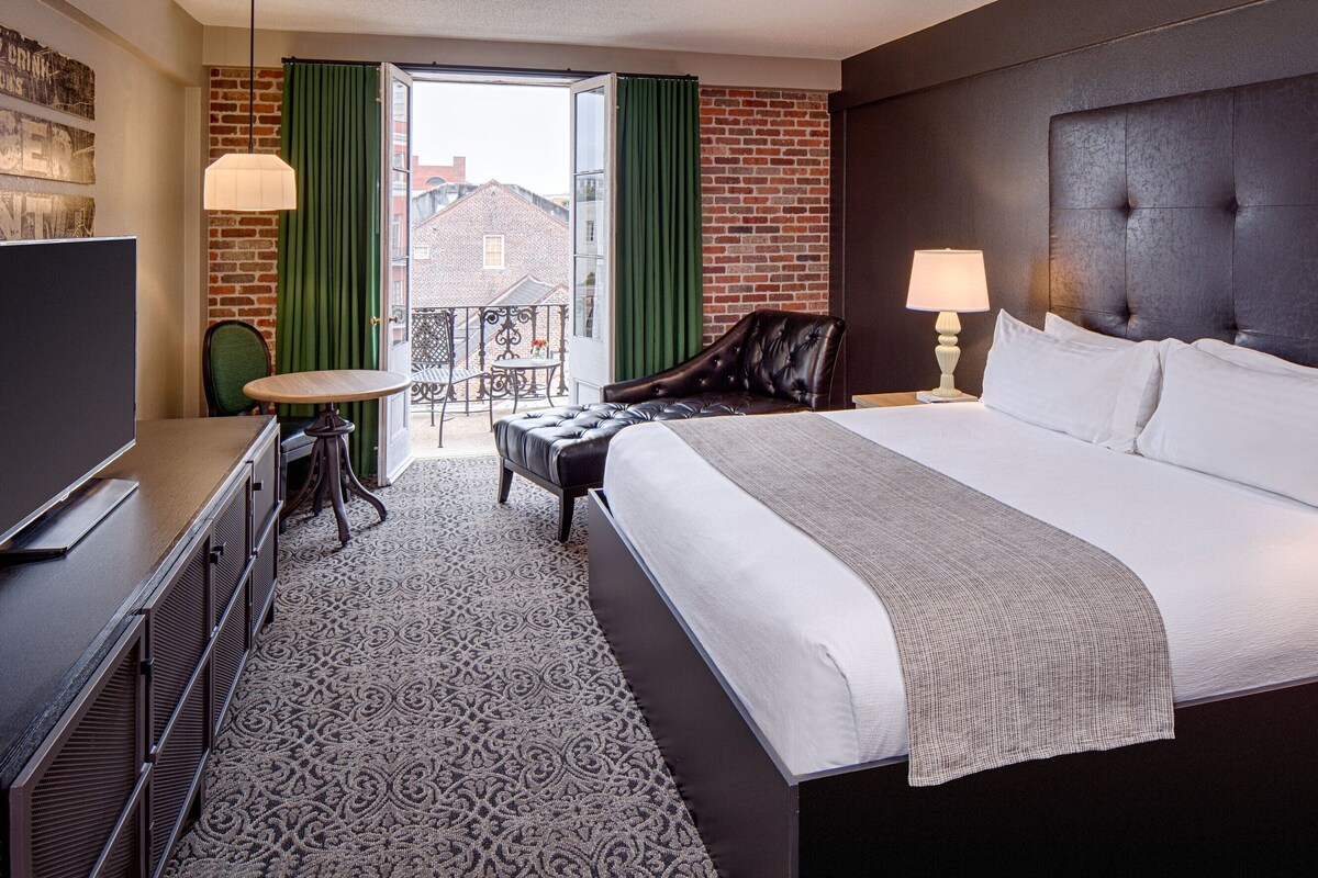 Une chambre d’hôtel avec un grand lit, une télévision, un bureau et un balcon agrémenté de rideaux verts.