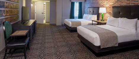 A hotel room with two beds, a desk, and a chair. There is a brick wall and a patterned carpet.