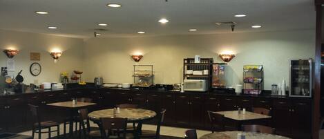 A hotel kitchen with multiple dining tables, a coffee machine, and a microwave.