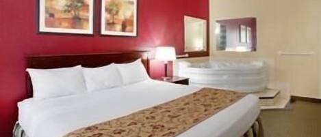A hotel room with a large bed, a red accent wall, and two framed pictures.