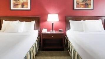 Una habitación de hotel con dos camas, una mesita de noche, una lámpara y dos cuadros en la pared.