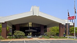 Un bâtiment moderne doté d'une entrée couverte, d'une enseigne indiquant « RAMADA » et d'un parking avec des places délimitées.