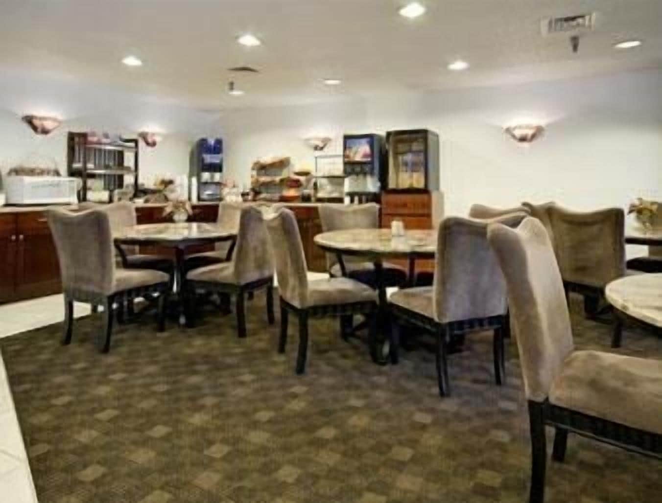 A dining area with multiple tables and chairs, a kitchen in the background, and a patterned carpet.