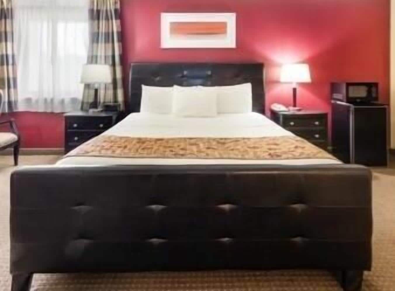 A hotel room with a large bed, a nightstand, a lamp, and a red wall.