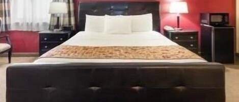 A hotel room with a large bed, a nightstand, a lamp, and a red wall.