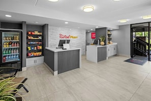 A modern reception area with a vending machine, a Red Roof Plus sign, and a reception desk. - Red Roof Inn PLUS+ Columbus-Ohio State University OSU (Columbus)