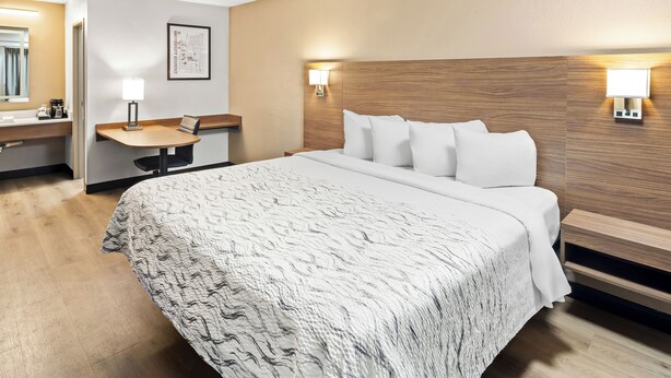 A hotel room with a large bed, a bedside table, a desk, a chair, a mirror, and two wall-mounted lamps. - Red Roof Inn PLUS+ Columbus-Ohio State University OSU (Columbus)