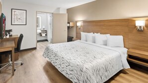 A hotel room with a large bed, a desk with a chair, a wooden headboard, and two wall-mounted lamps. - Red Roof Inn PLUS+ Columbus-Ohio State University OSU (Columbus)