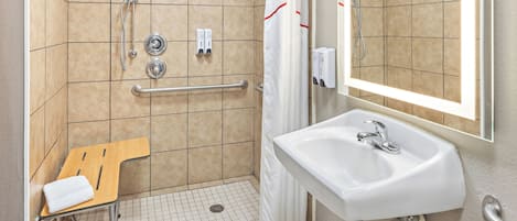 A bathroom with a shower, a sink, a hand dryer, a towel rack, and a grab bar.