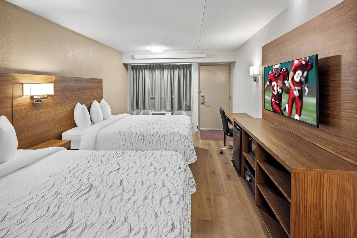 Hotellihuone, jossa on kaksi sänkyä, seinälle asennettu televisio, työpöytä ja ikkuna, jossa on verhot.