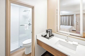 A modern bathroom with a glass shower enclosure, a white toilet, a coffee maker on the vanity, and a large mirror reflecting the room. - Red Roof Inn PLUS+ Columbus-Ohio State University OSU (Columbus)