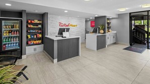 A modern reception area with a vending machine, a Red Roof Plus sign, and a reception desk.